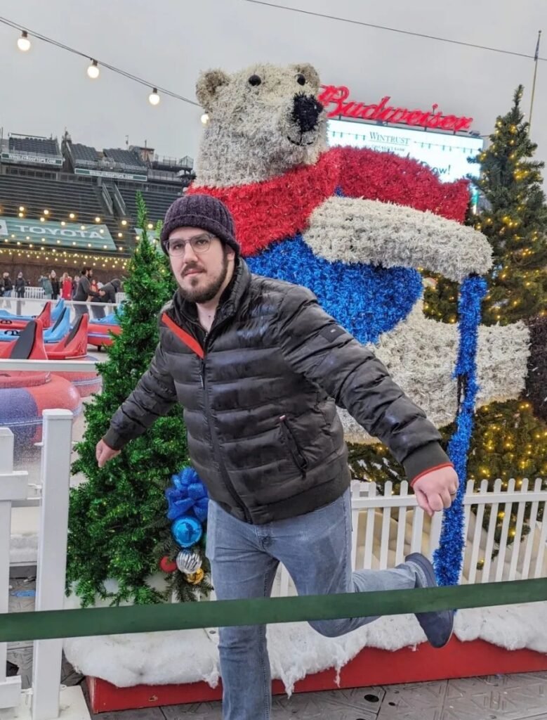 A picture of Keanan, dressed in a winter coat in front of a statue of a polar bear, making the same pose as the polar bear.